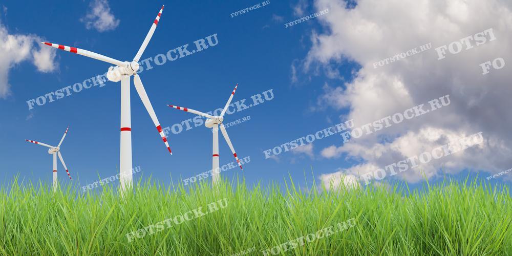 Фотография изображает несколько ветряных турбин, установленных среди зелёной травы на фоне голубого неба с облаками. Снимок подчеркивает гармоничное сочетание возобновляемой энергии и природной среды.